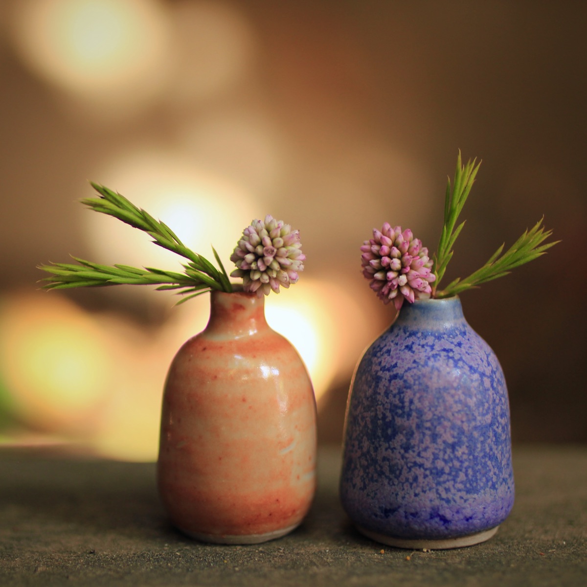 Two miniature bud vases holding pink blossoms and grasses, one glazed coral and cream, the other speckled blue